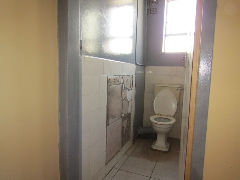 A small, dated bathroom featuring a toilet, tiled flooring, and partially tiled walls in need of repair and modernization.