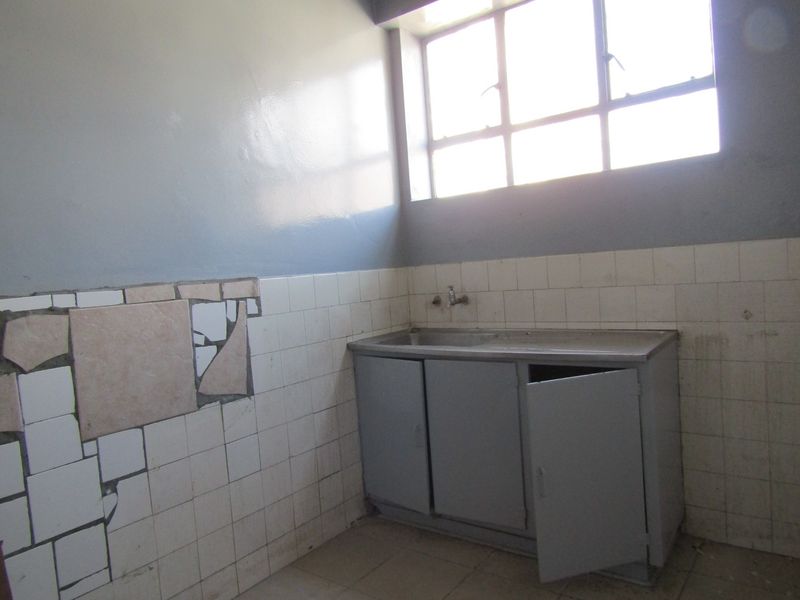 A utility or laundry area featuring a stainless steel sink, built-in metal cabinetry, and a window, currently requiring significant repair to wall tiles and cabinetry.
