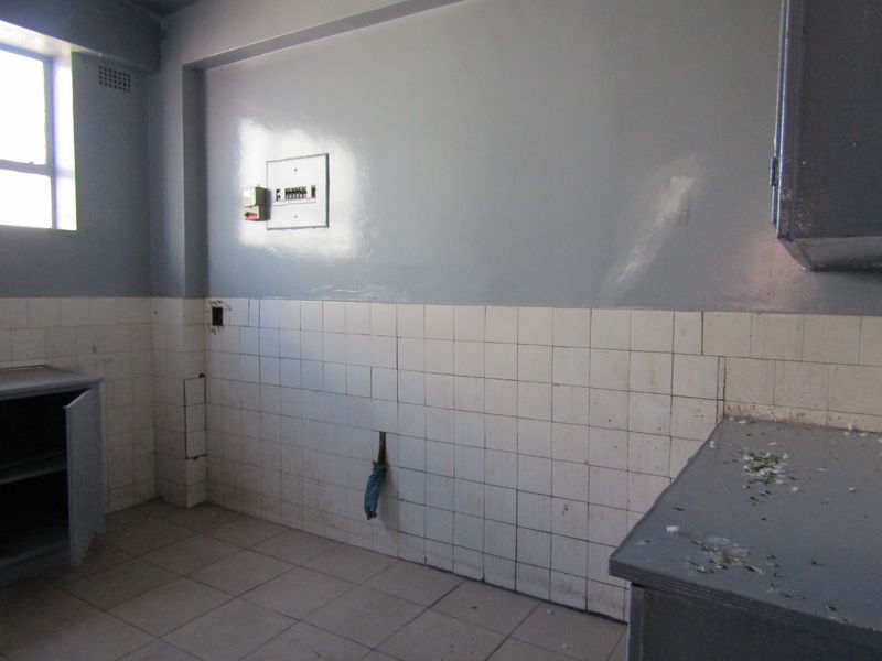 A vacant kitchen area featuring tiled splashbacks, built-in cabinetry, and an electrical distribution board, requiring cosmetic updates and repairs.