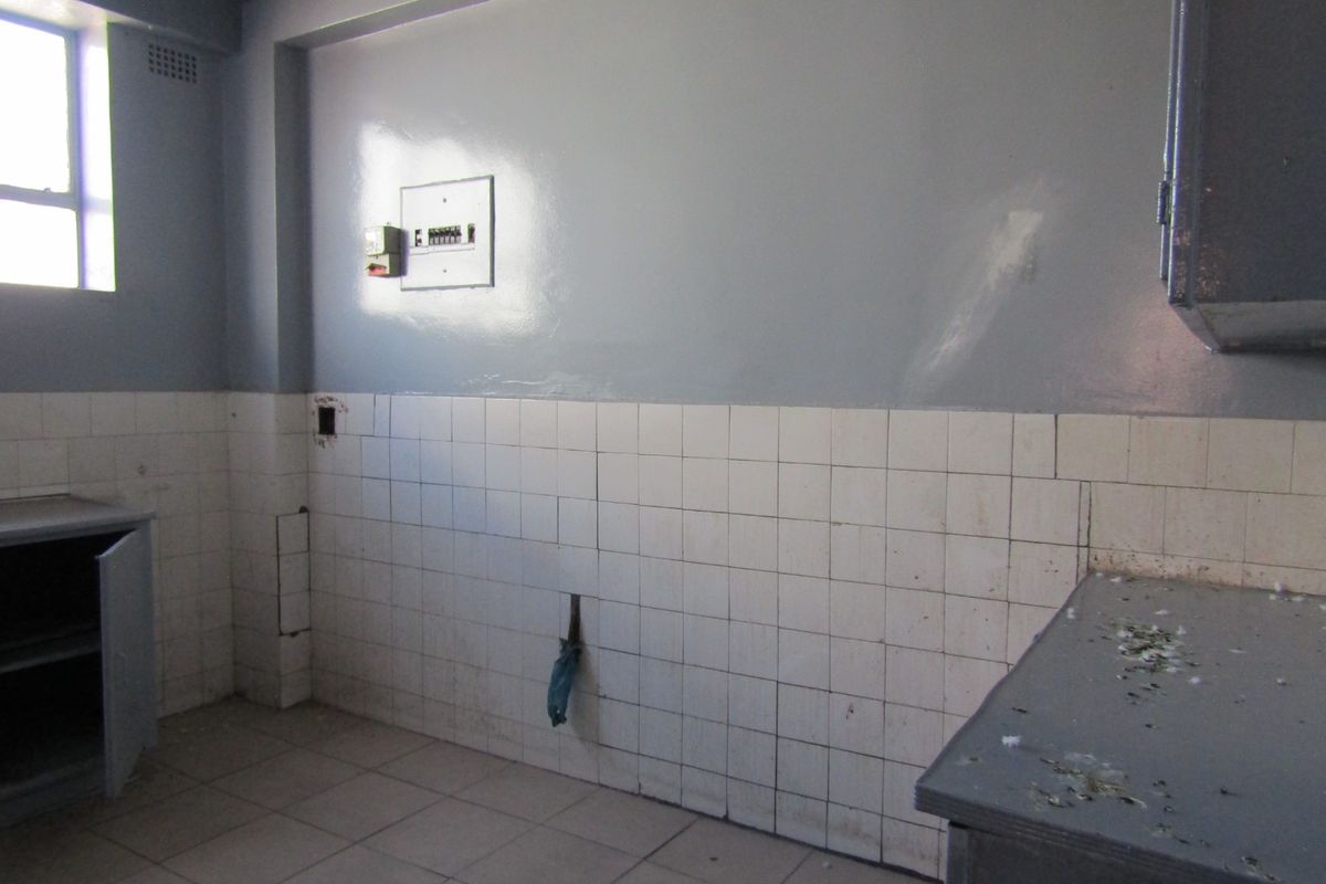A vacant kitchen area featuring tiled splashbacks, built-in cabinetry, and an electrical distribution board, requiring cosmetic updates and repairs.