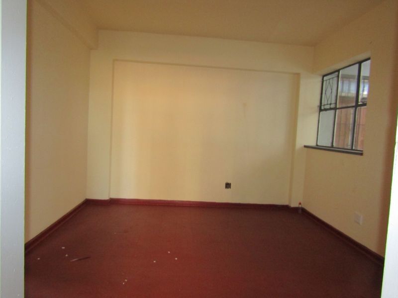 An empty living room featuring painted walls, steel-framed windows, and a solid floor finish, offering a blank canvas for renovation.