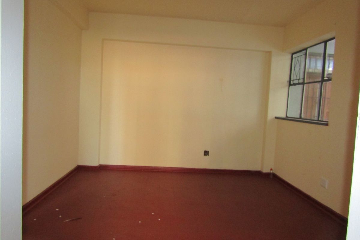 An empty living room featuring painted walls, steel-framed windows, and a solid floor finish, offering a blank canvas for renovation.