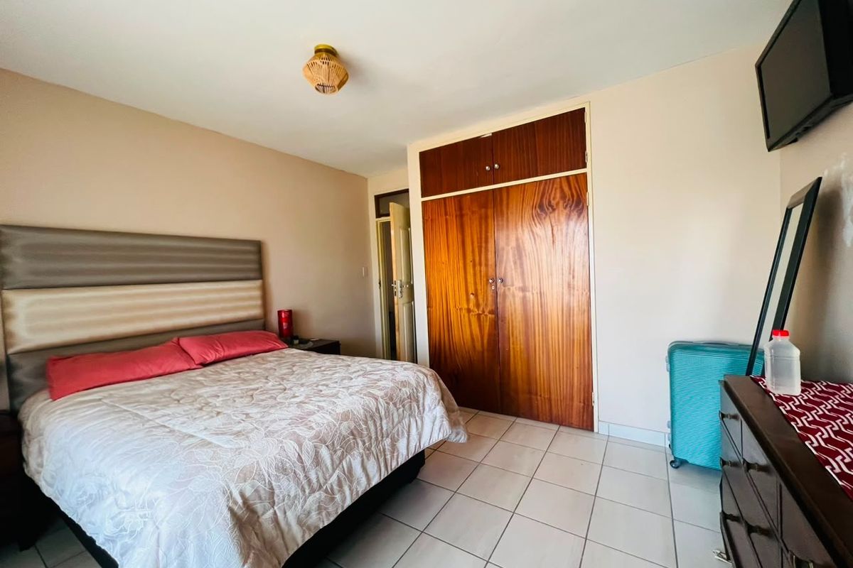 A bedroom featuring tiled flooring and a large built-in wooden wardrobe, providing functional storage space.