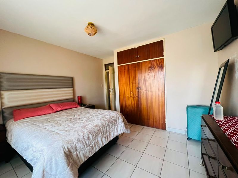 A bedroom featuring tiled flooring and a large built-in wooden wardrobe, providing functional storage space.