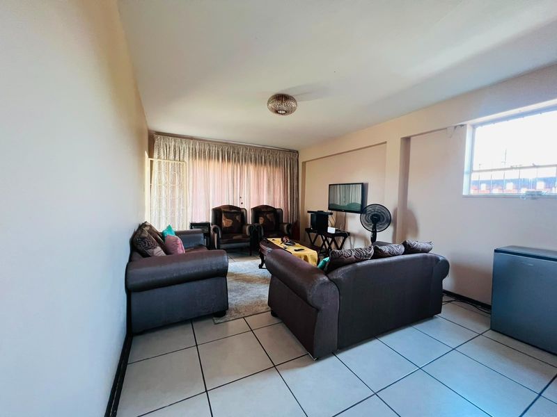 A living room featuring tiled flooring and large windows with curtain tracks, offering a functional space for relaxation.