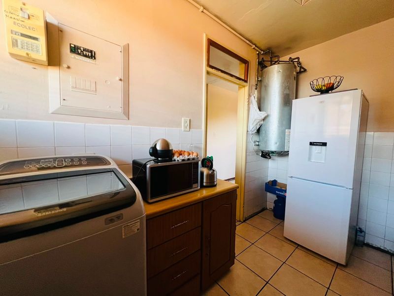 Functional laundry area featuring tiled flooring, built-in cabinetry, wall-mounted electrical distribution board, and an exposed geyser unit.