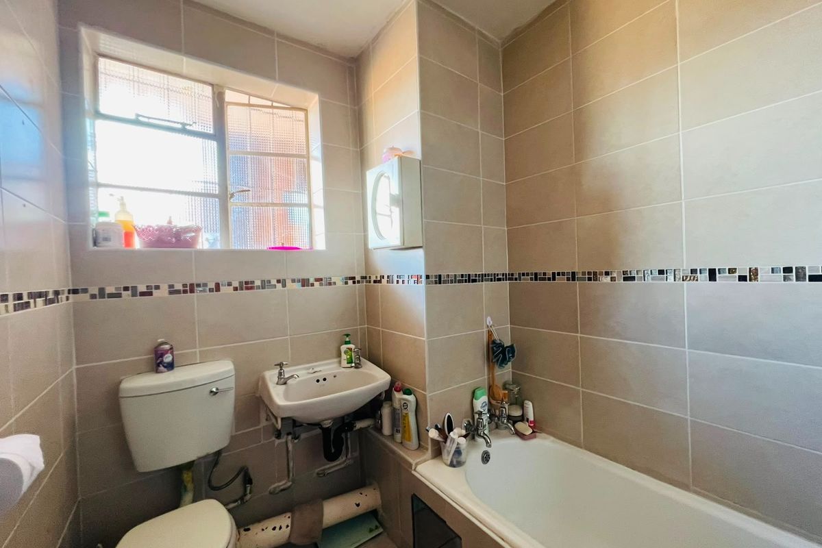 A functional bathroom featuring full-height wall tiling with a mosaic accent, a standard bathtub, wall-mounted basin, and toilet with exposed plumbing.