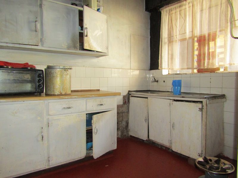 A dated kitchen featuring original built-in cabinetry, a tiled backsplash, and a stainless steel sink, requiring significant renovation and cosmetic updates.