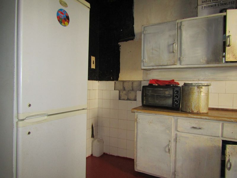 A dated kitchen area featuring worn cabinetry, a tiled backsplash with missing tiles, and damaged wall surfaces requiring renovation.