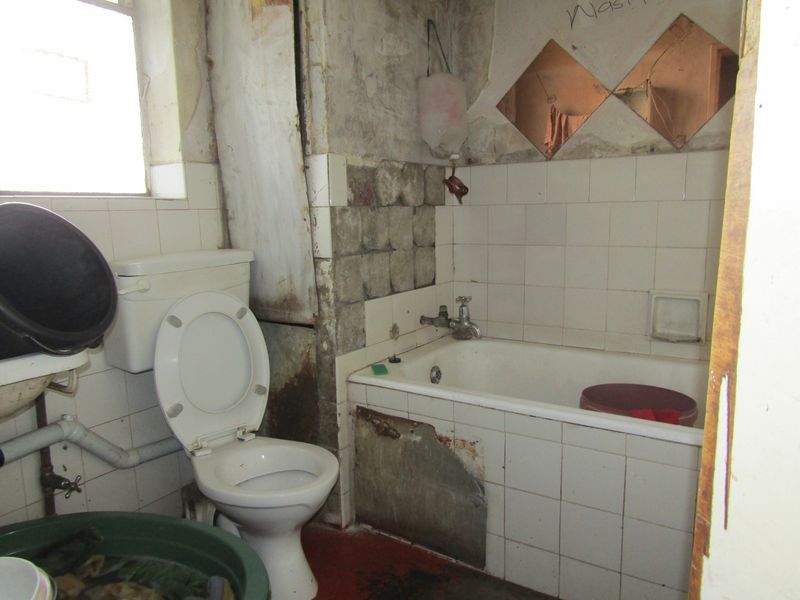 A bathroom in need of significant renovation, featuring a bathtub, toilet, and tiled walls with visible damage to the finishes and structure.