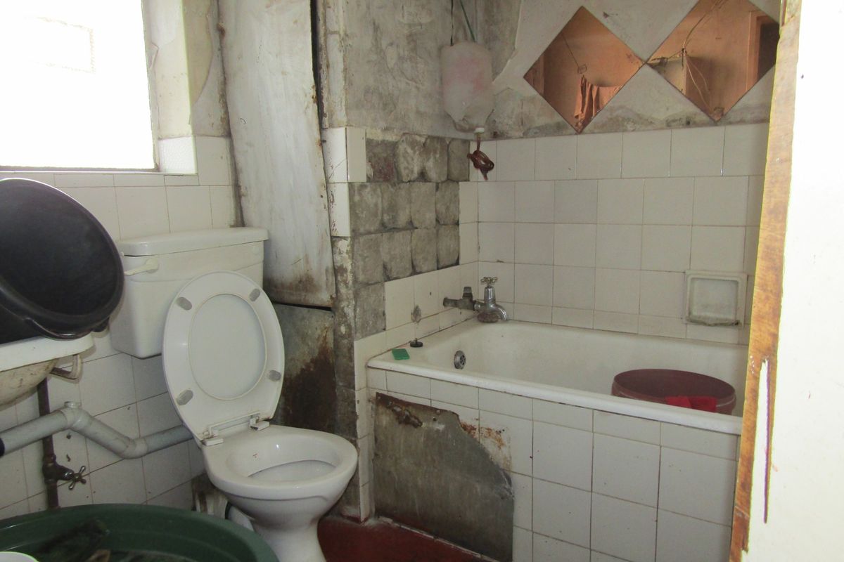 A bathroom in need of significant renovation, featuring a bathtub, toilet, and tiled walls with visible damage to the finishes and structure.