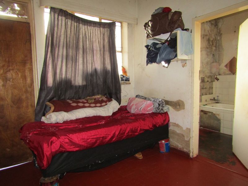 A bedroom in poor condition showing significant wall damage and staining, with an adjacent bathroom visible through the doorway.