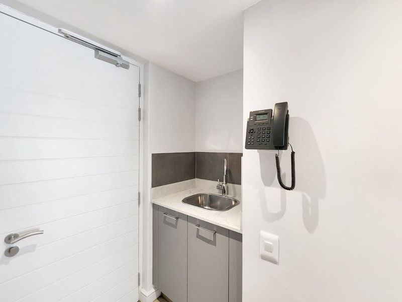 A compact utility area featuring built-in cabinetry, a stone countertop with an integrated stainless steel sink, and a tiled splashback.
