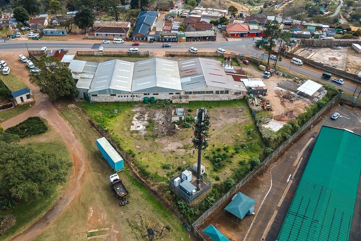 Aerial view of an industrial property featuring a large warehouse, telecommunications tower, and surrounding yard space with paved access and perimeter fencing.