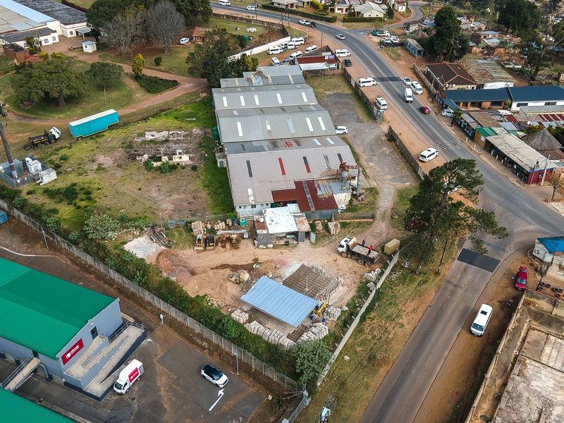 Aerial view of an industrial property featuring a warehouse building, perimeter fencing, and an unpaved yard area with direct road access.