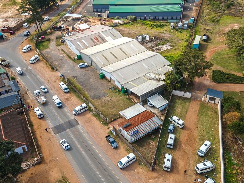 Aerial view of an industrial property featuring a large warehouse building, paved yard area, and perimeter fencing with direct street access.