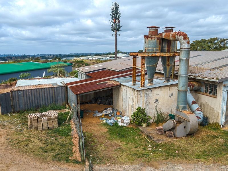 Aerial view of an industrial facility featuring a large external cyclone dust extraction system, corrugated metal roofing, and a roller shutter door.