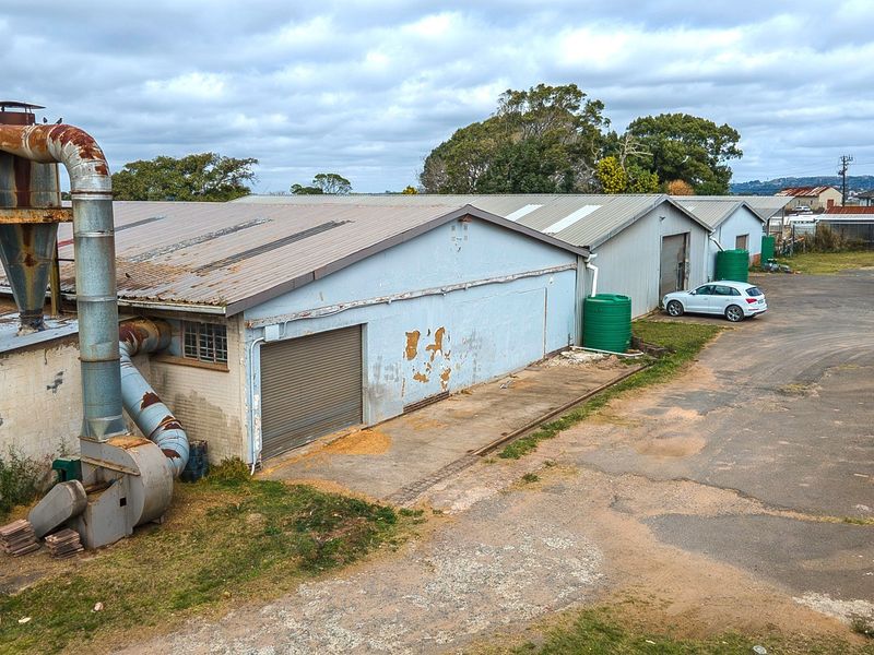 Aerial view of an industrial property featuring metal-clad warehouse buildings, external ventilation infrastructure, water tanks, and a large concrete yard area.