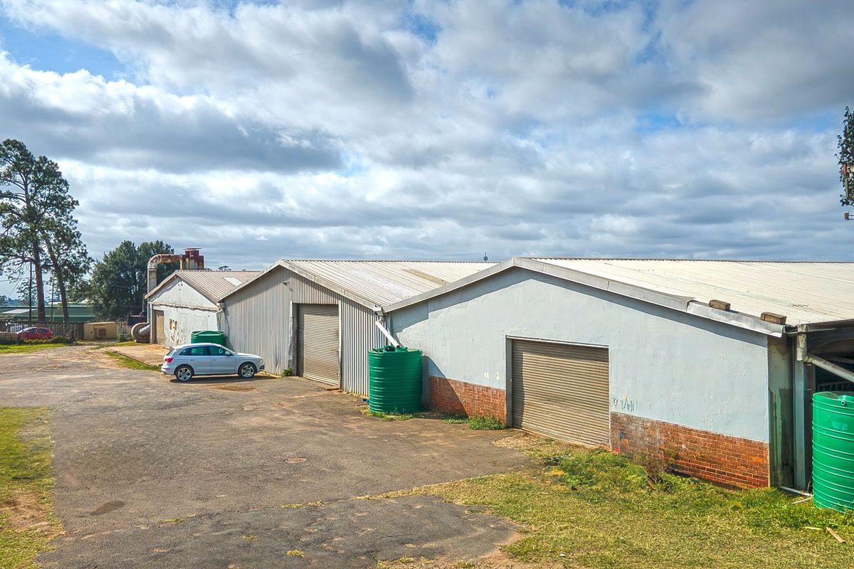 Rear view of an industrial property featuring corrugated metal roofing, multiple roller shutter doors, and external water storage tanks set within a paved yard.