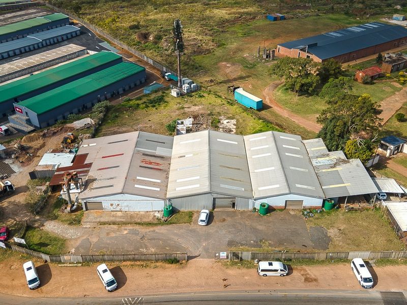 Aerial view of an industrial warehouse facility featuring a large corrugated metal roof, paved yard space, and perimeter fencing on a spacious site.