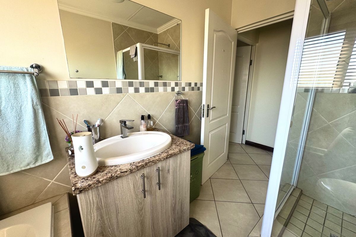 A functional bathroom featuring a vanity with granite countertop, basin, wall-mounted mirror, and a separate shower enclosure with tiled finishes.