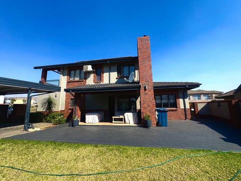 Rear view of a two-story brick house featuring a covered patio, paved outdoor area, and a prominent brick chimney.