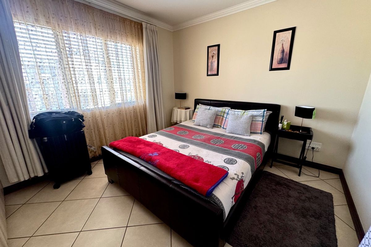 A well-lit bedroom featuring neutral wall tones, tiled flooring, and large windows with fitted curtains, providing a comfortable and functional living space.