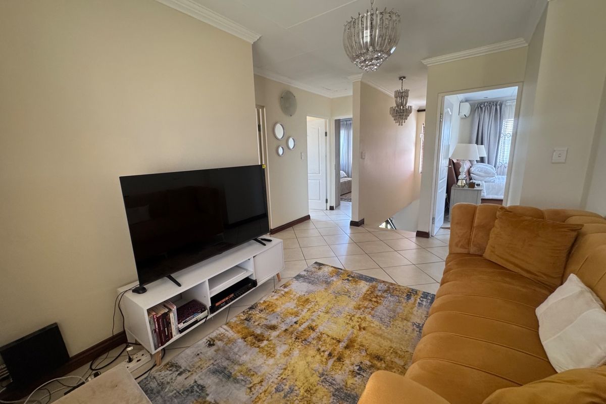 A well-maintained living area featuring ceramic tile flooring, decorative crown molding, and elegant crystal chandeliers, providing access to adjacent rooms.