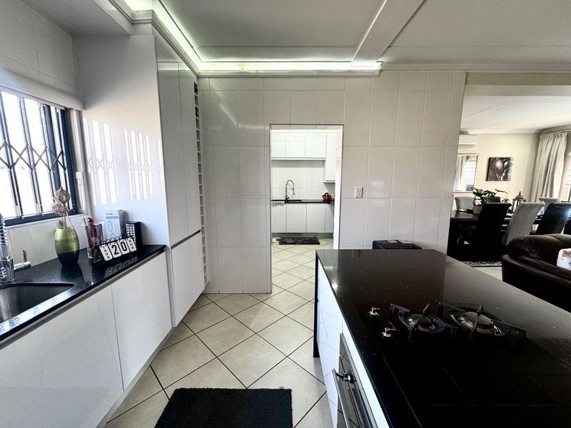 Modern kitchen featuring sleek white cabinetry, contrasting black granite countertops, a gas hob, and an integrated oven, with an adjacent scullery area.