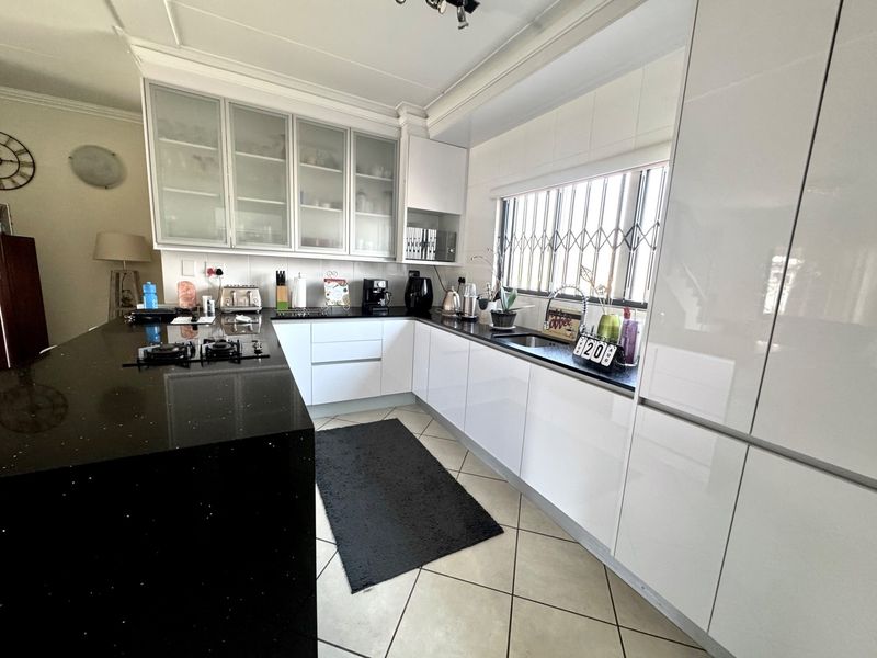 Modern kitchen featuring high-gloss white cabinetry, contrasting black granite countertops, a gas hob, and ample storage with glass-fronted display cabinets.