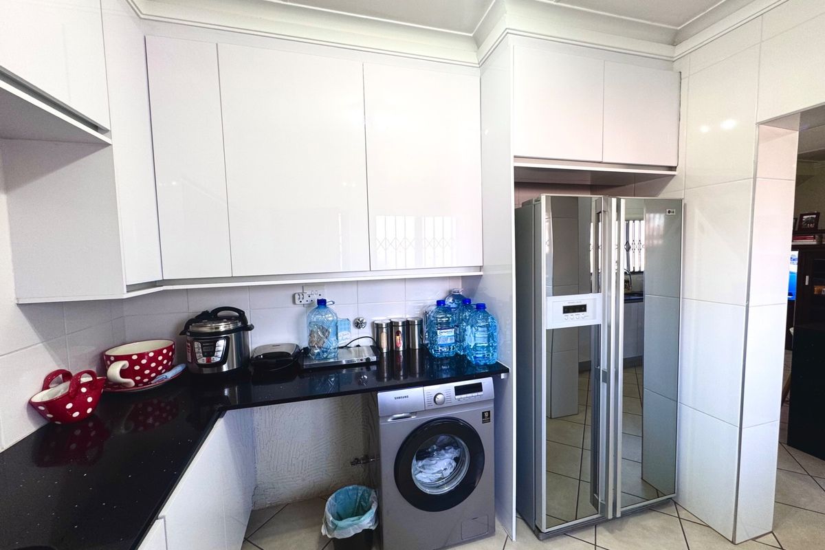 Modern kitchen featuring high-gloss white cabinetry, black granite countertops, tiled backsplash, and integrated space for laundry appliances.