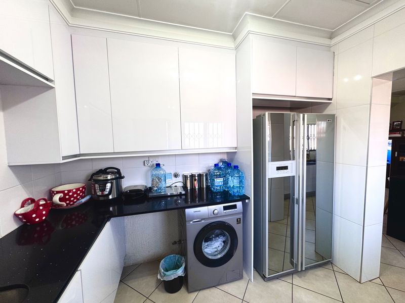 Modern kitchen featuring high-gloss white cabinetry, black granite countertops, tiled backsplash, and integrated space for laundry appliances.