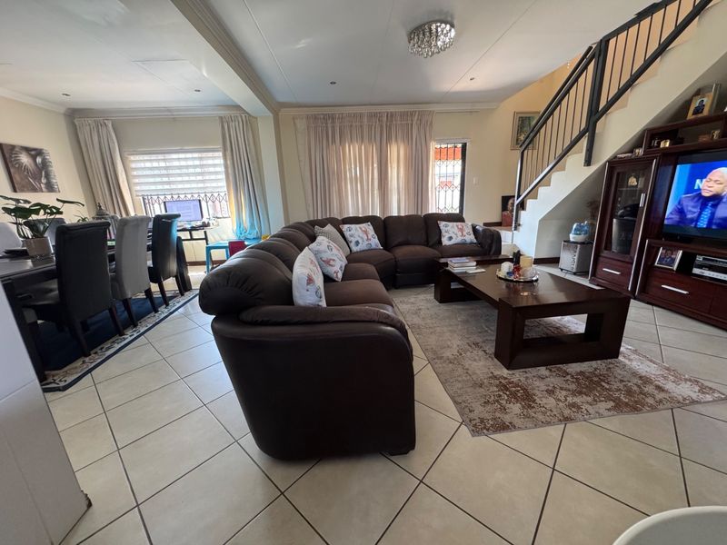 Spacious open-plan living and dining area featuring tiled flooring, a central staircase with metal balustrades, and modern recessed lighting.