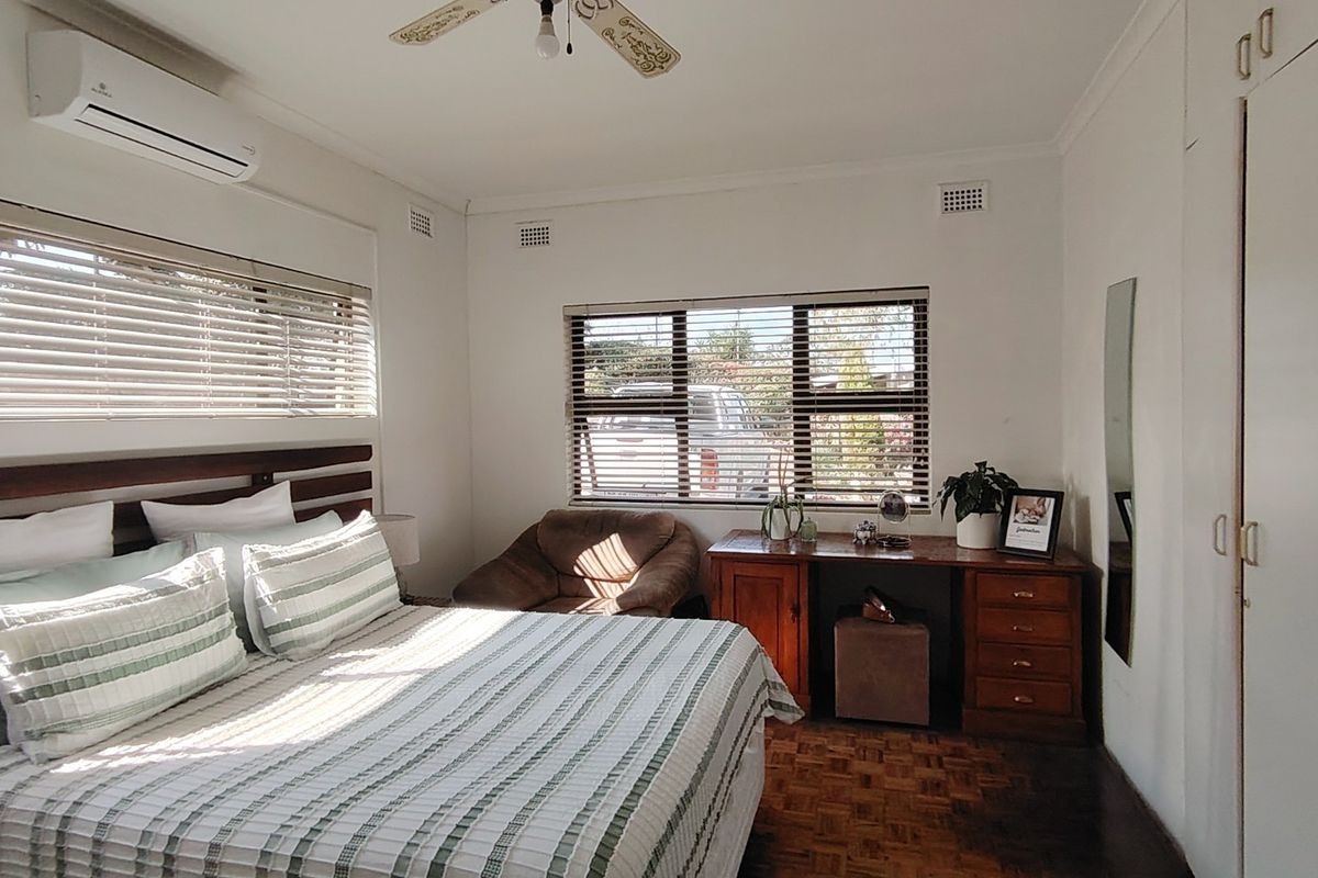 A well-lit bedroom featuring parquet flooring, built-in cupboards, an air conditioning unit, and a ceiling fan.