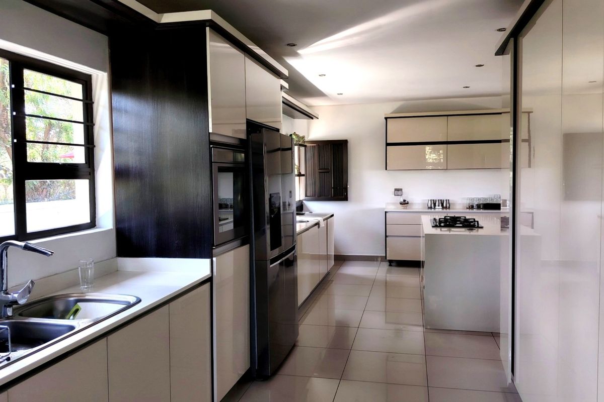 Modern kitchen featuring sleek high-gloss cabinetry, stone countertops, integrated appliances, a gas hob, and large windows providing ample natural light.