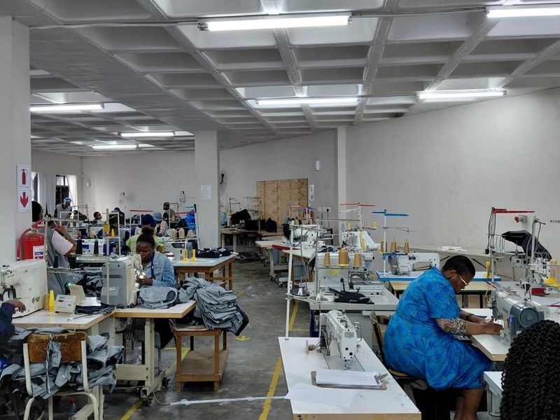 A spacious industrial workshop area featuring a waffle slab ceiling, fluorescent lighting, and concrete flooring, currently utilized as a garment manufacturing facility.