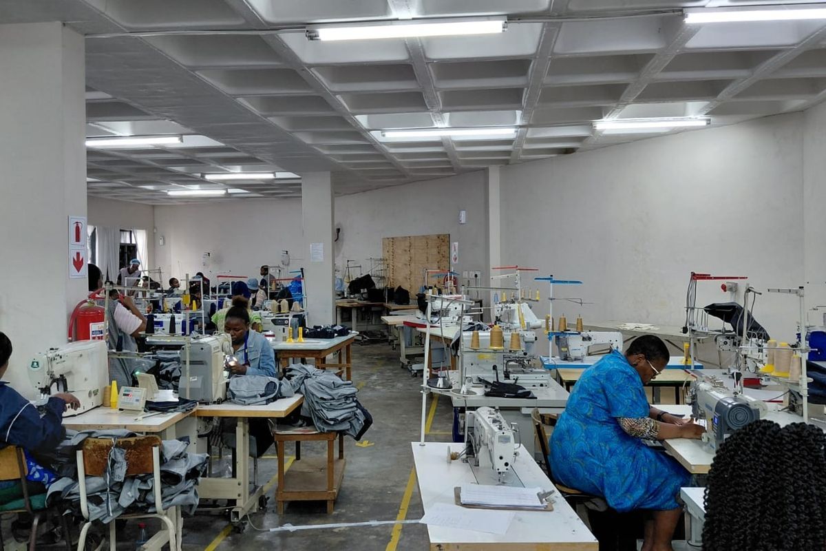 A spacious industrial workshop area featuring a waffle slab ceiling, fluorescent lighting, and concrete flooring, currently utilized as a garment manufacturing facility.