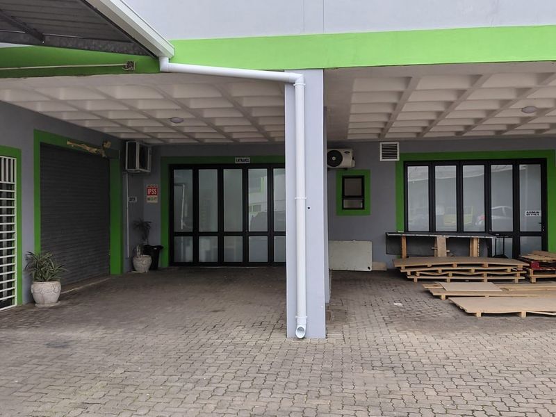 Industrial property exterior featuring a paved driveway, covered entrance area, roller shutter door, and multiple access points with aluminium framed glass doors.