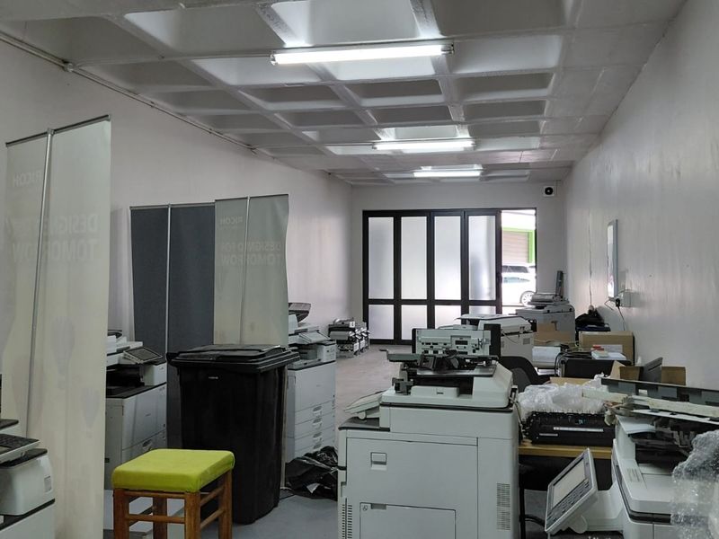 Industrial office space featuring a waffle slab ceiling, fluorescent lighting, and a glass panelled entrance door.
