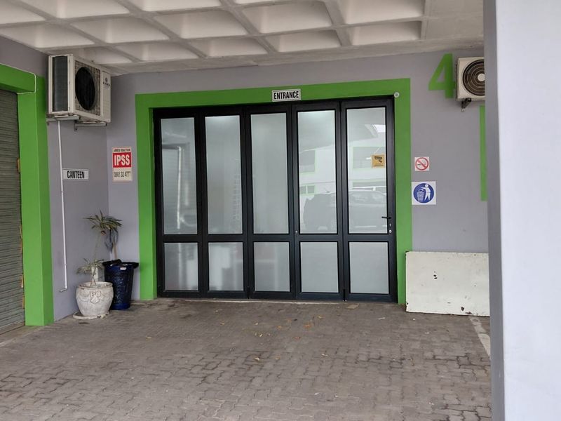 Industrial entrance area featuring a paved exterior, aluminium framed glass doors, and a waffle slab ceiling with an integrated air conditioning unit.