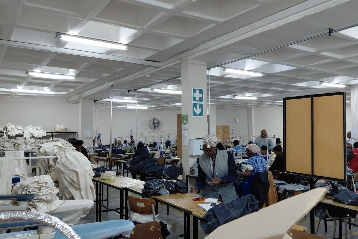 A large industrial workspace featuring a coffered ceiling, overhead fluorescent lighting, and structural support columns, currently utilized as a garment manufacturing facility.