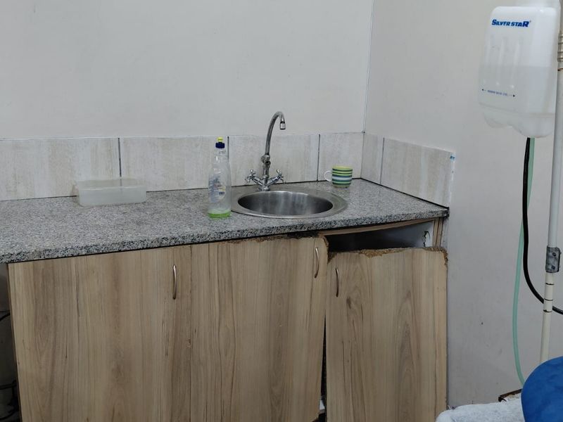 Utility area featuring a granite countertop, stainless steel sink, and tiled backsplash, currently showing significant wear to the base cabinetry.
