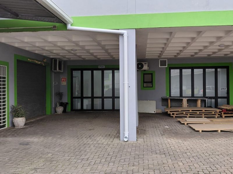 Industrial property exterior featuring a paved driveway, covered entrance area, roller shutter door, and multiple access points with aluminum-framed glass doors.