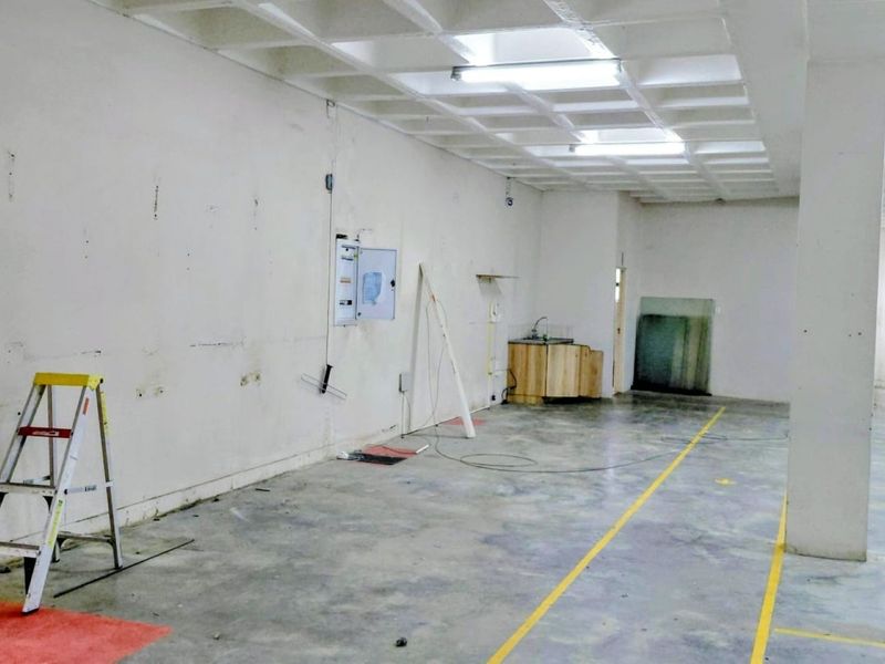 Spacious industrial utility area featuring a waffle slab ceiling, concrete flooring, and a basic kitchenette sink unit, suitable for various commercial or storage uses.