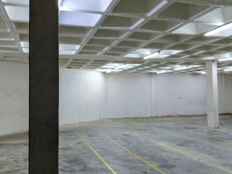 Spacious industrial utility area featuring a distinctive waffle slab ceiling, concrete flooring, and functional overhead fluorescent lighting, suitable for storage or workshop use.