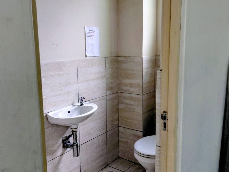 A functional industrial-style bathroom featuring a wall-mounted basin and toilet with neutral ceramic wall tiling.