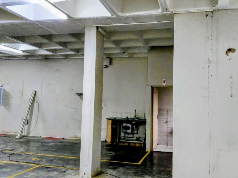 Open-plan industrial utility space featuring a waffle slab ceiling, concrete flooring, a small kitchenette area, and an integrated electrical distribution board.