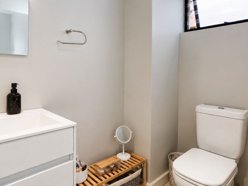 A clean and modern bathroom featuring a white vanity cabinet with basin, wall-mounted mirror, and a standard toilet.