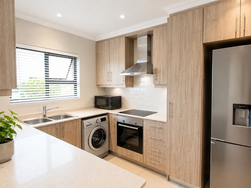 Modern kitchen featuring light wood-grain cabinetry, stone countertops, subway tile backsplash, and integrated stainless steel appliances including an oven, hob, and extractor fan.