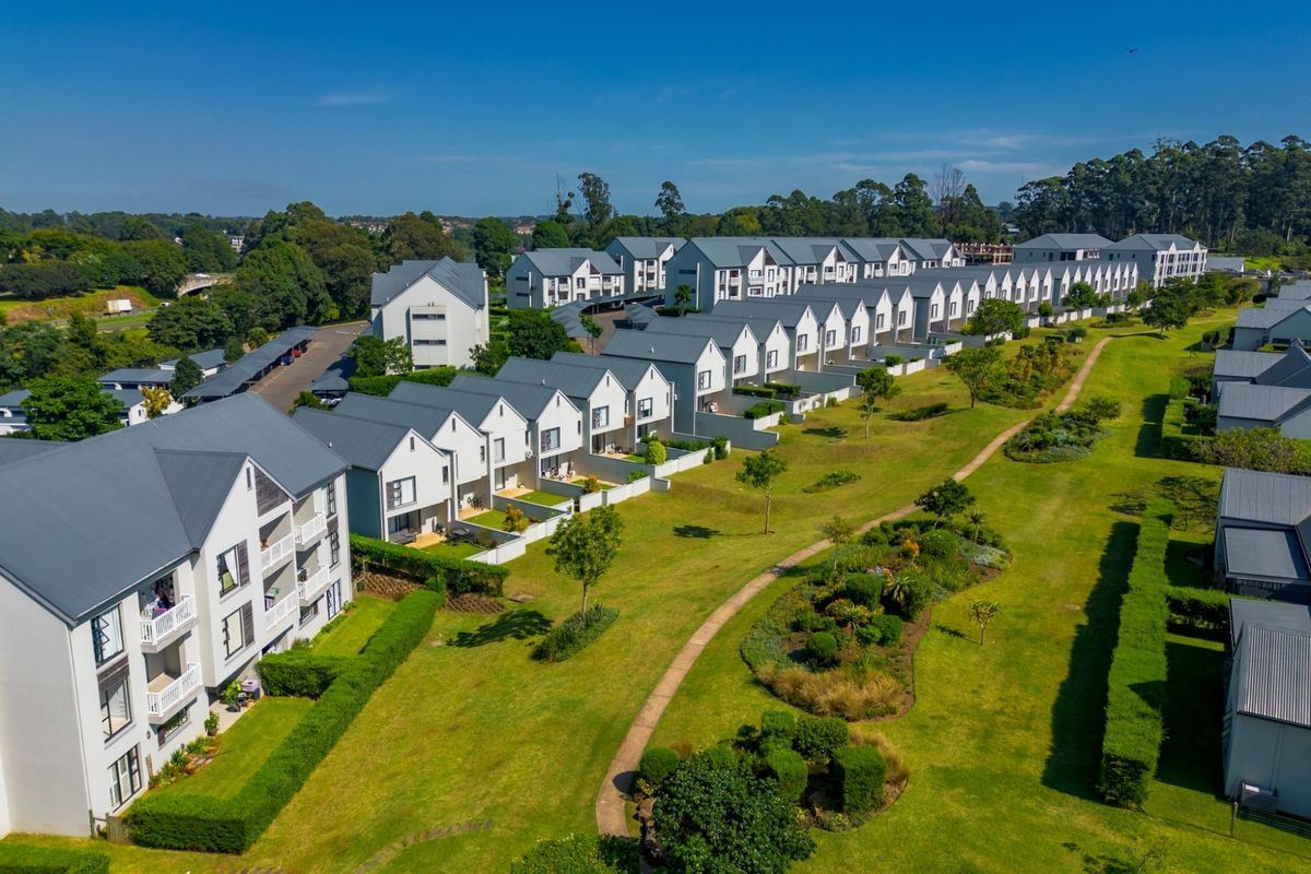 Aerial view of a residential apartment complex featuring multiple buildings with pitched roofs, surrounded by well-maintained communal gardens and paved pathways.